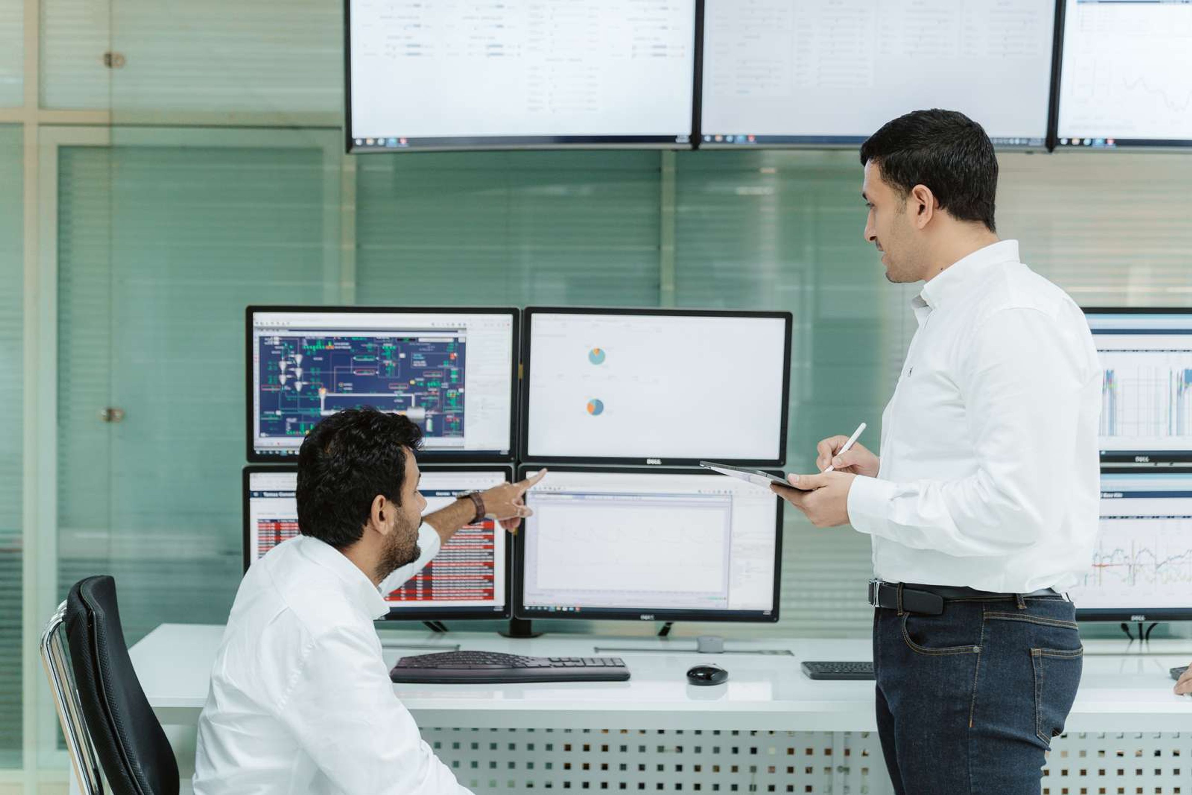 Two engineers reviewing process data on multiple monitors in a control room