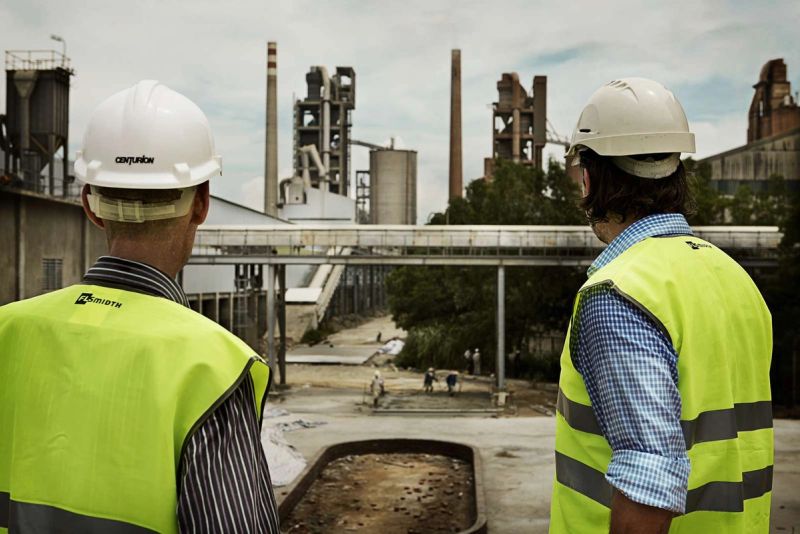 Construction workers observing cement plant operations from a distance