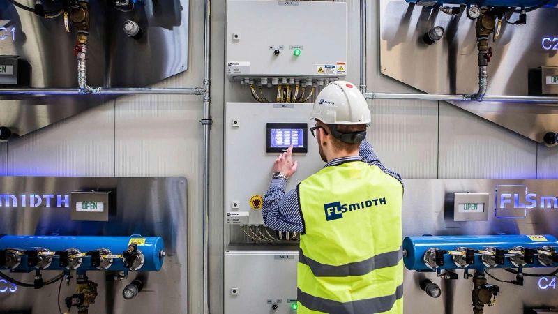 FLSmidth technician operating a touchscreen control panel in an industrial plant environment